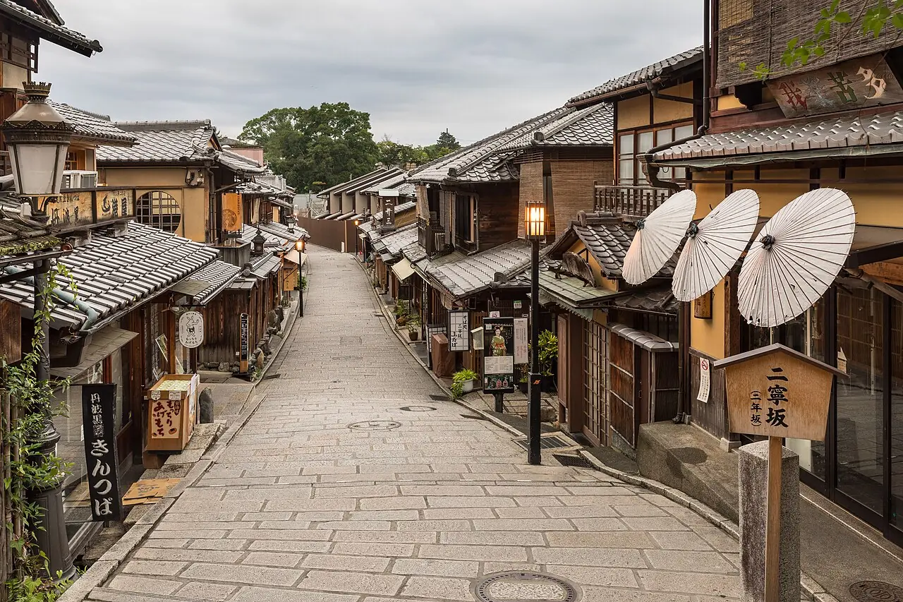 A stone-paved lane of old wooden shops in Kyoto's Higashiyama, with paper parasols outside a shop